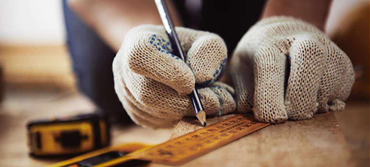 Close-up of craftsman hands in protective gloves measuring woode